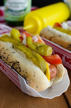 two hotdogs with pickles, tomatoes and mustard in buns on a table