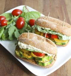 two sandwiches with tomatoes, lettuce and other vegetables on a white platter