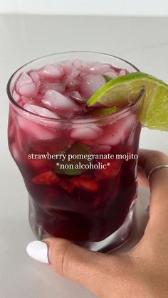 a hand holding a glass filled with red liquid and lime wedged into the rim