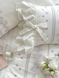 white flowers are laying on the bed next to pillows and a perfume bottle with a pink label