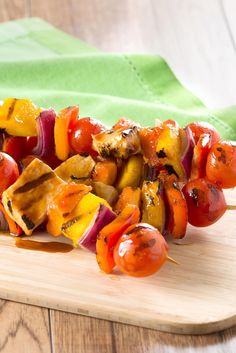 a wooden cutting board topped with meat and veggies on skewered skewers