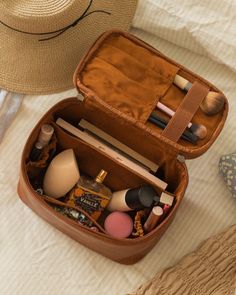 an open suitcase sitting on top of a bed next to a hat and other items