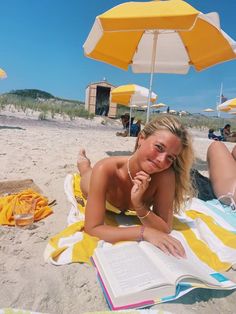 a woman laying on top of a beach next to an open book and yellow umbrella