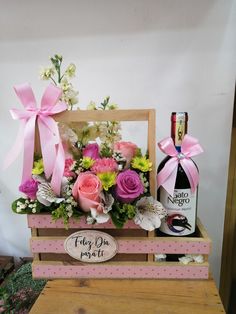 a wooden crate filled with pink and white flowers next to a bottle of booze