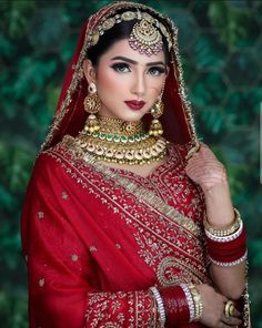 a woman wearing a red and gold bridal outfit with jewelry on her head, in front of a green background