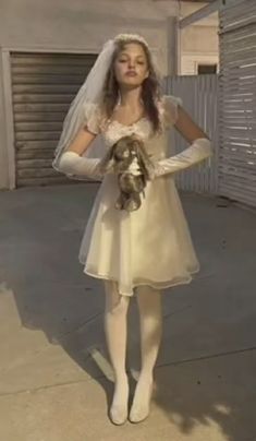 a woman in a white wedding dress holding a teddy bear wearing a veil and gloves