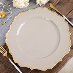 a white plate with gold trim sits on a wooden table next to silverware and flowers