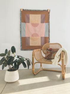 a chair sitting next to a potted plant in front of a wall hanging