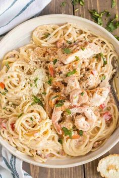 a white bowl filled with pasta and meat on top of a wooden table next to bread