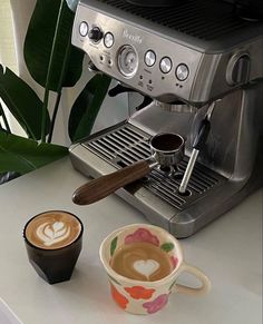 two cups of coffee sit on a counter next to an espresso machine