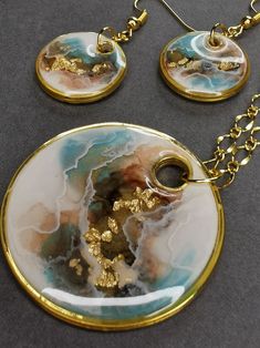 a necklace and earring set with gold leaf designs on it, sitting on a gray surface