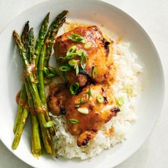 a white plate topped with chicken and asparagus next to rice on top of a table