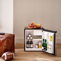 an open refrigerator with drinks and footballs on the floor next to it in a living room