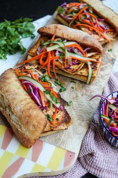 two sandwiches with veggies are on a cutting board next to a bowl of salad