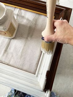 a person holding a paint brush over a white frame