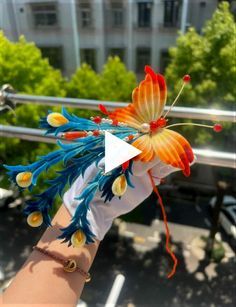 a woman's hand holding an orange and blue butterfly on top of her arm