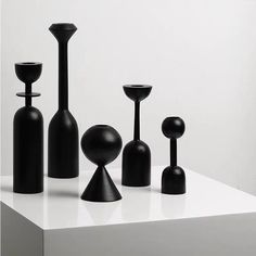 several black vases and candles on a white surface