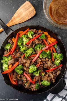 beef and broccoli stir fry in a skillet next to a bowl of gravy