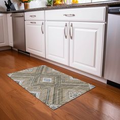 a kitchen with white cabinets and wooden floors, an area rug is on the floor