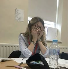 a woman sitting at a table in front of a water bottle with her hands on her face