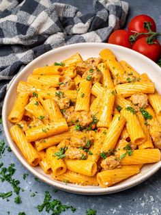 a bowl full of pasta with meat and parsley on the side next to tomatoes