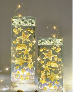 two clear glass vases with gold stars and moon decorations on them, lit up by fairy lights