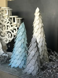 three paper christmas trees sitting on top of a table next to silver and white decorations