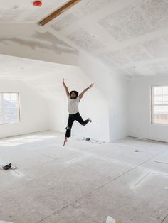 a person jumping in the air with their arms up and legs spread wide, while wearing black pants and a white t - shirt