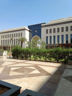 an empty courtyard in front of a building with many trees and bushes on both sides