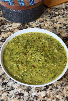 a white bowl filled with green soup on top of a counter next to a bottle