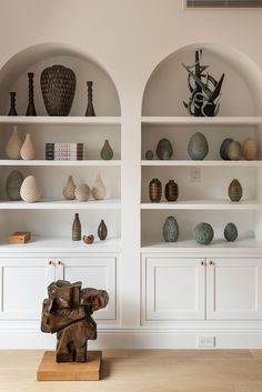 two white shelves with vases and sculptures on them in front of each other's bookshelves