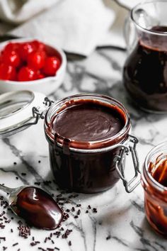 chocolate spread in glass jars with spoons and cherries on the table next to them