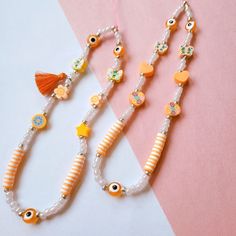 two necklaces on a pink and white striped surface with an orange tassel hanging from it