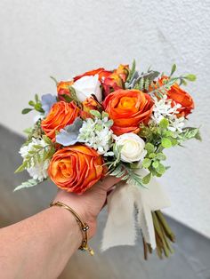 an orange and white bridal bouquet being held by a woman's hand in front of a wall