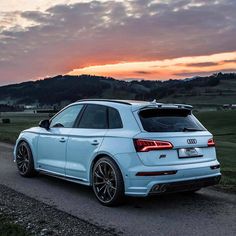 the rear end of a white car driving down a country road at sunset with hills in the background