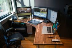 a desk with two laptops and three monitors on top of it next to a window