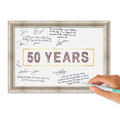 a hand holding a pen in front of a 50th birthday sign with writing on it