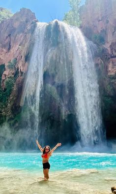 a woman standing in front of a waterfall with her arms up and hands out to the side