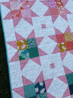 a pink and white quilt with stars on the top is laying on some green grass