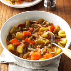 two bowls filled with vegetable soup on top of a wooden table next to silverware