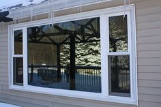 an open window on the side of a house with snow on the ground and trees in the background