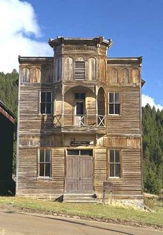 an old wooden building sitting on the side of a road in front of a forest