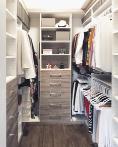 a walk in closet filled with lots of white and wood furniture, including clothes hanging on shelves