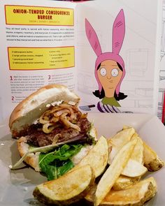 a burger and french fries are sitting on a plate next to an open cookbook