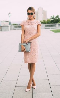 a woman in a pink lace dress holding a gray purse and posing for the camera