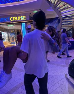 two people hugging each other in front of a carousel at the mall, while others are walking around