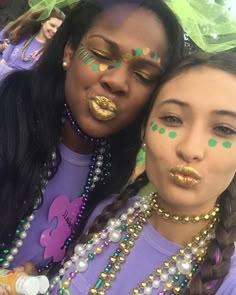 two young women with face paint and beads on their faces, one is holding her arm around the other's neck