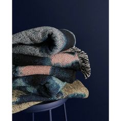 two blankets stacked on top of each other in front of a dark blue background with a stool