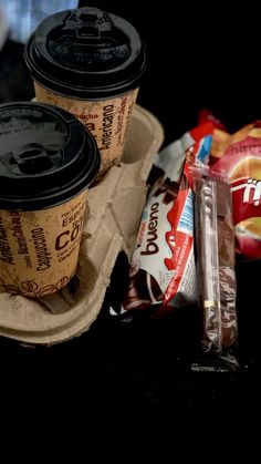 coffee cups sitting on top of a carton next to some chips and bagels