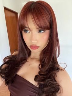 a woman with long red hair wearing a brown dress and posing for the camera in front of a mirror